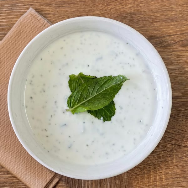 A white bowl of creamy yogurt dip with green herbs and two fresh mint leaves on top.